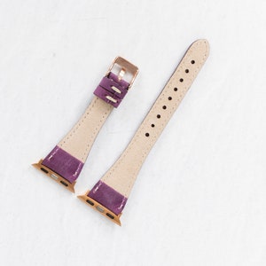 May include: Two purple leather watch bands with rose gold hardware. The bands are designed for Apple Watches.