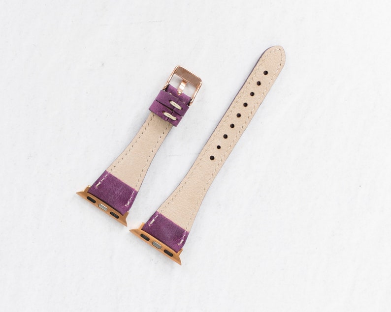 May include: Two purple leather watch bands with rose gold hardware. The bands are designed for Apple Watches.