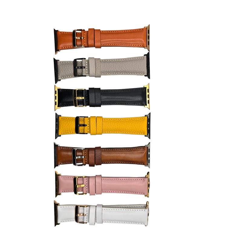 K&ouml;nnte beinhalten: Eine Auswahl an Leder-Armb&auml;ndern in verschiedenen Farben, darunter Orange, Grau, Schwarz, Gelb, Braun, Rosa und Wei&szlig;. Jedes Armband verf&uuml;gt &uuml;ber eine Schnalle und Anschl&uuml;sse f&uuml;r eine Apple Watch. Die Armb&auml;nder sind vor wei&szlig;em Hintergrund dargestellt.