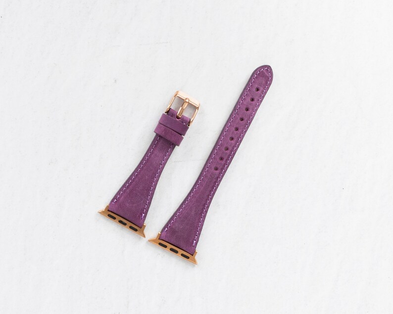 May include: Two purple leather watch bands with gold hardware. The bands are designed for Apple Watches.