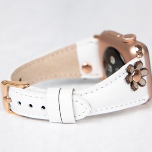 Pode incluir: Pulseira de rel&oacute;gio de couro branco com fivela de ouro rosa e um pequeno detalhe floral. A pulseira &eacute; compat&iacute;vel com Apple Watch.
