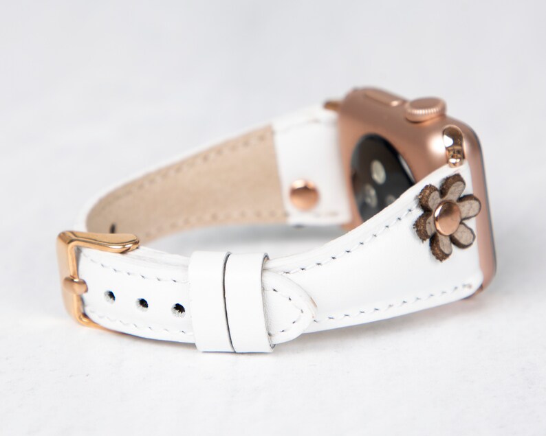 Pode incluir: Pulseira de rel&oacute;gio de couro branco com fivela de ouro rosa e um pequeno detalhe floral. A pulseira &eacute; compat&iacute;vel com Apple Watch.