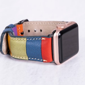 Puede incluir: Una correa de reloj de cuero colorida con rayas verdes, azules, rojas y moradas. La correa est&aacute; unida a un Apple Watch de oro rosa.
