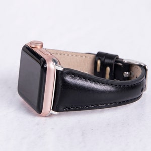 May include: A black leather watch strap with a rose gold Apple Watch.