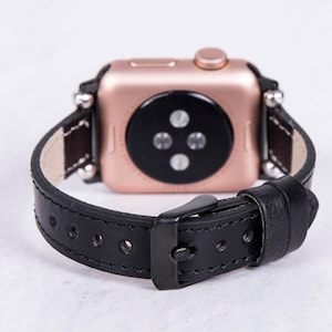 Puede incluir: Una correa de reloj de cuero negro con un Apple Watch de oro rosa. La correa tiene un cierre de hebilla y est&aacute; dise&ntilde;ada para un reloj de 42 mm o 44 mm.