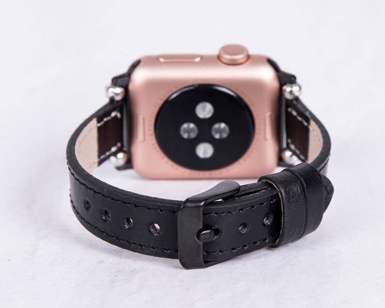 Puede incluir: Una correa de reloj de cuero negro con un Apple Watch de oro rosa. La correa tiene un cierre de hebilla y est&aacute; dise&ntilde;ada para un reloj de 42 mm o 44 mm.