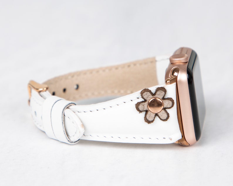 Pode incluir: Pulseira de rel&oacute;gio Apple de couro branco com fivela de ouro rosa e um pequeno design floral.