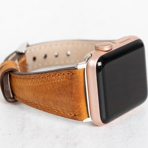 May include: A brown leather watch strap with a rose gold Apple Watch.