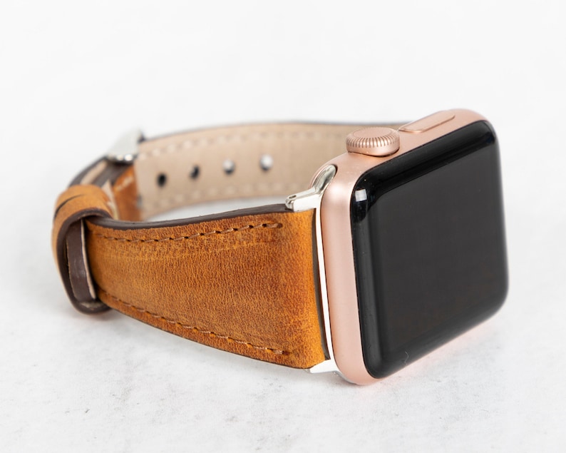 May include: A brown leather watch strap with a rose gold Apple Watch.