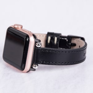 Puede incluir: Un Apple Watch de oro rosa con una correa de cuero negro. La esfera del reloj es negra y la correa tiene un borde cosido.