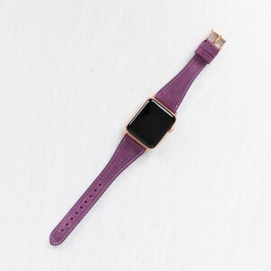 May include: A purple leather watch band with a rose gold buckle and a black watch face.