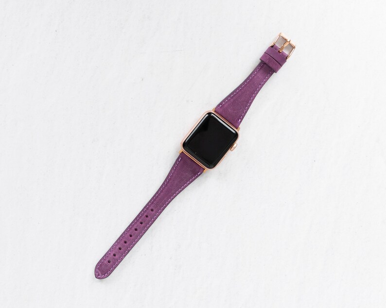 May include: A purple leather watch band with a rose gold buckle and a black watch face.
