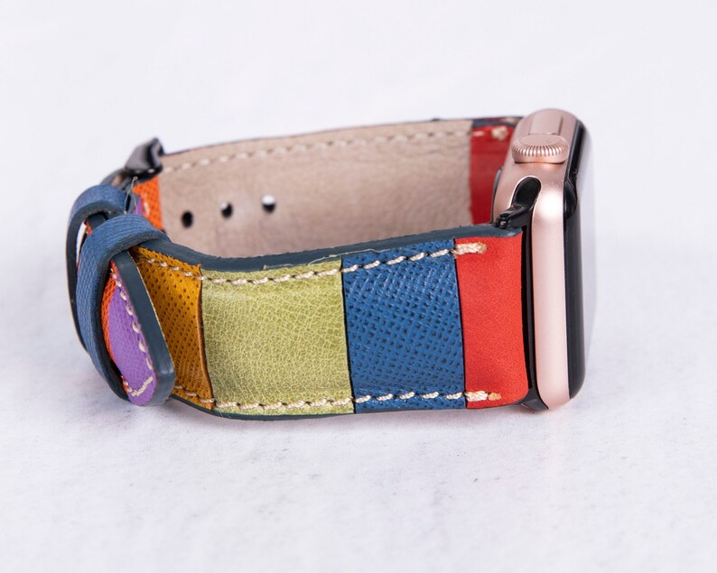 Puede incluir: Una correa de reloj de cuero colorida con rayas de morado, naranja, verde, azul y rojo. La correa est&aacute; unida a un Apple Watch de oro rosa.