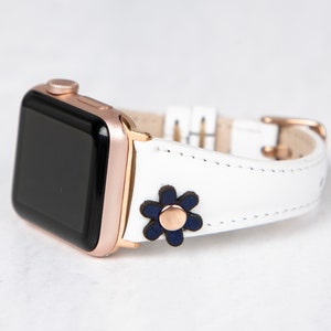 Pode incluir: Pulseira de rel&oacute;gio Apple de couro branco com fivela de ouro rosa e um detalhe de flor azul marinho.