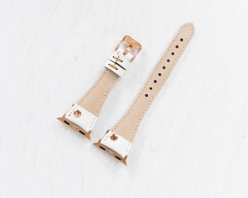 Pode incluir: Duas pulseiras de rel&oacute;gio de couro branco com ferragens de ouro rosa. As pulseiras s&atilde;o projetadas para Apple Watches.