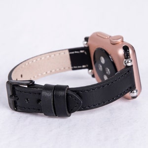 Puede incluir: Una correa de reloj de cuero negro con un Apple Watch de oro rosa. La correa tiene un cierre de hebilla y est&aacute; dise&ntilde;ada para un reloj de 38 mm o 40 mm.