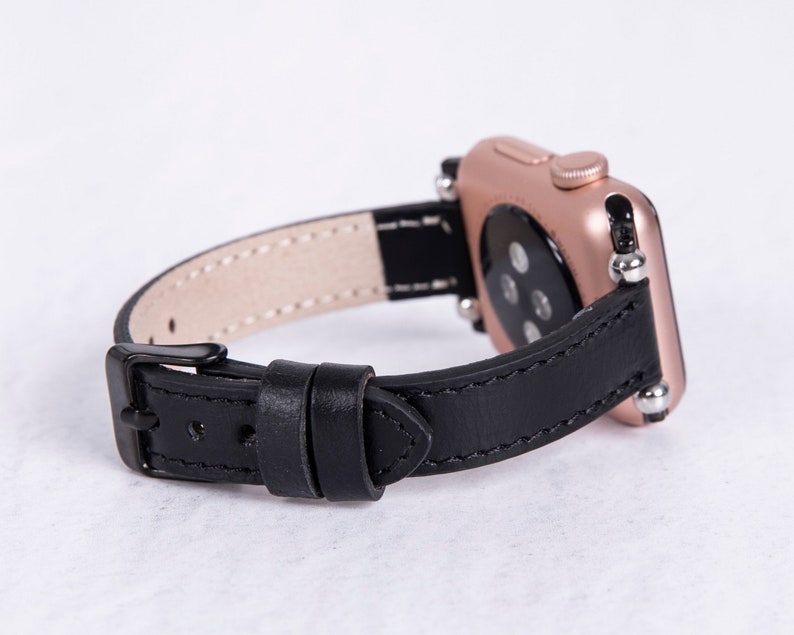 Puede incluir: Una correa de reloj de cuero negro con un Apple Watch de oro rosa. La correa tiene un cierre de hebilla y est&aacute; dise&ntilde;ada para un reloj de 38 mm o 40 mm.