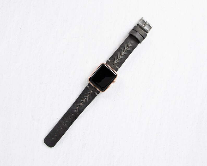 May include: A black leather Apple Watch strap with a silver buckle and a geometric pattern. The strap is designed for a rose gold Apple Watch.
