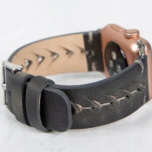 A close-up view of a gray leather Apple Watch band attached to a rose gold watch case, showing the side profile and silver buckle.