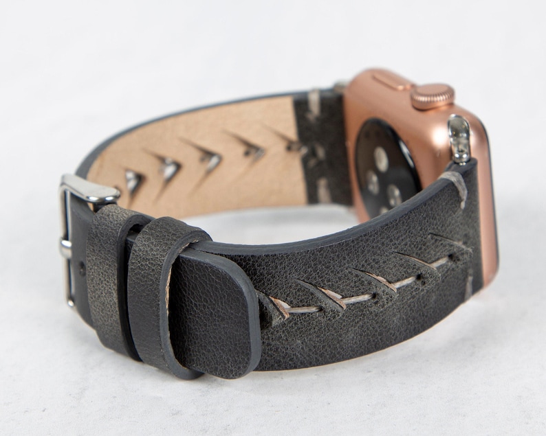 A close-up view of a gray leather Apple Watch band attached to a rose gold watch case, showing the side profile and silver buckle.