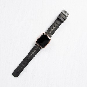A full-length overhead shot of the gray leather watch band and rose gold Apple Watch laid out straight on a white surface.