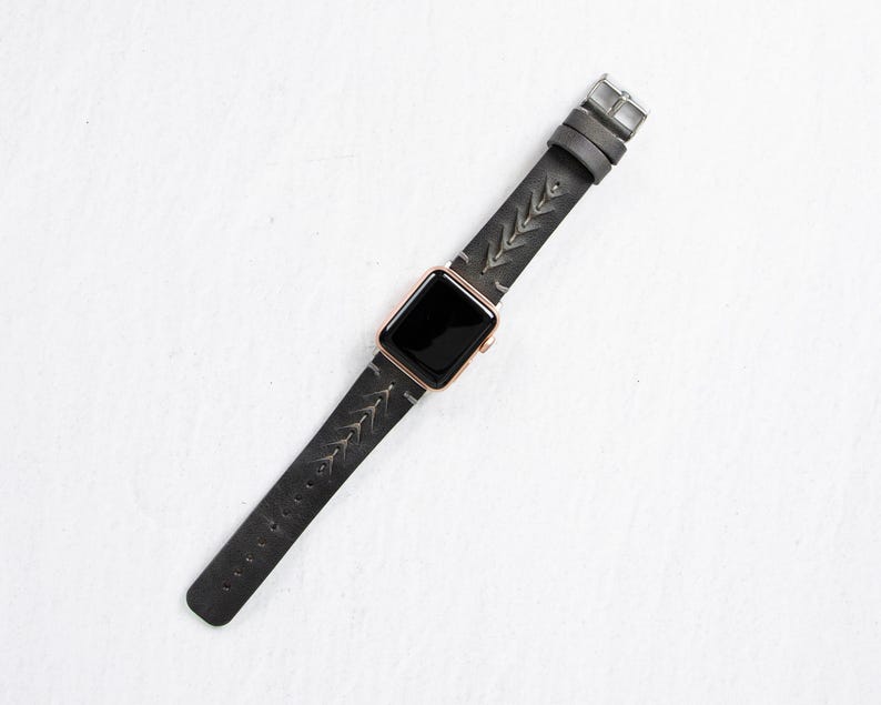 A full-length overhead shot of the gray leather watch band and rose gold Apple Watch laid out straight on a white surface.