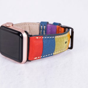 Puede incluir: Un Apple Watch de oro rosa con una banda de cuero multicolor. La banda tiene rayas de cuero rojo, azul, verde y morado.