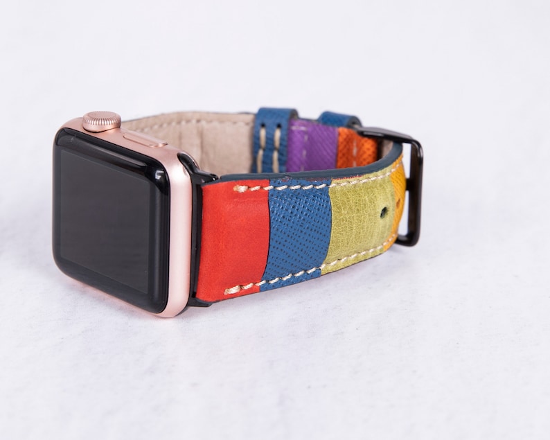 Puede incluir: Un Apple Watch de oro rosa con una banda de cuero multicolor. La banda tiene rayas de cuero rojo, azul, verde y morado.