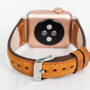 May include: A brown leather watch strap with a rose gold Apple Watch face. The strap has a buckle fastening and is designed for a 40mm or 44mm Apple Watch.