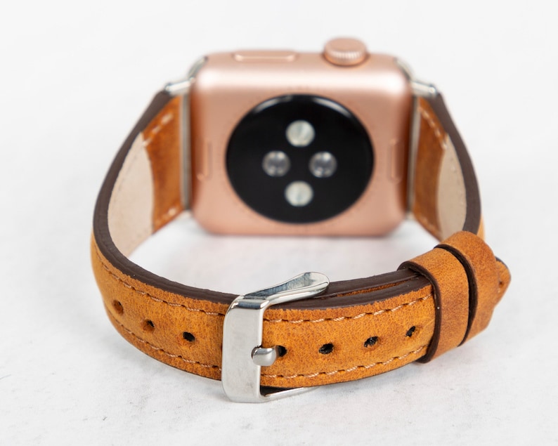 May include: A brown leather watch strap with a rose gold Apple Watch face. The strap has a buckle fastening and is designed for a 40mm or 44mm Apple Watch.
