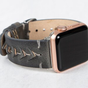 An angled view of the gray leather watch band attached to a rose gold Apple Watch with a black screen.