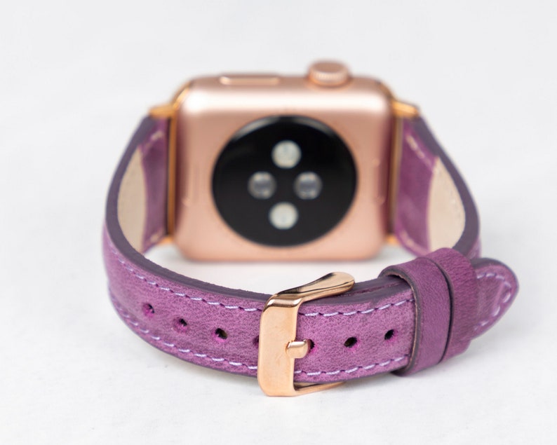 May include: A purple leather watch band with a rose gold buckle and a rose gold Apple Watch face.