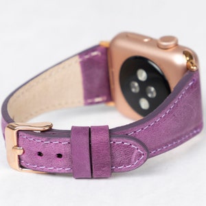 May include: A purple leather watch band with a rose gold watch face and buckle. The band has a textured finish and white stitching.