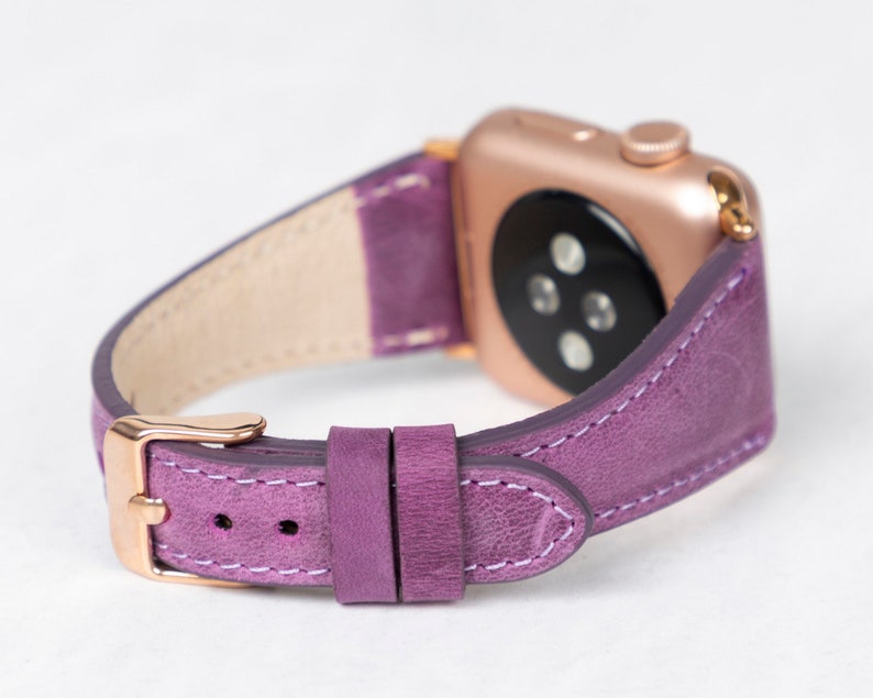May include: A purple leather watch band with a rose gold watch face and buckle. The band has a textured finish and white stitching.