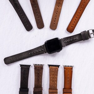 An assortment of leather watch bands in various colors including black, brown, and tan surrounding a central gray band attached to a smart watch.