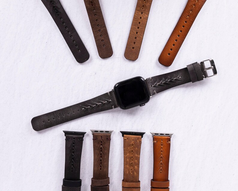 An assortment of leather watch bands in various colors including black, brown, and tan surrounding a central gray band attached to a smart watch.