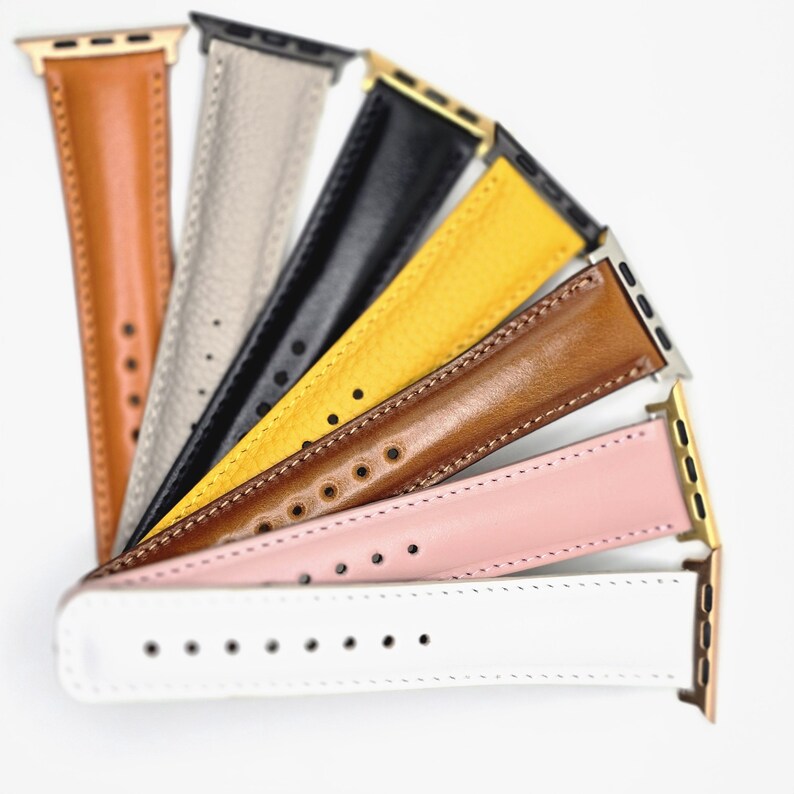 K&ouml;nnte beinhalten: Eine Auswahl an Leder-Armb&auml;ndern in verschiedenen Farben: Hellbraun, Grau, Schwarz, Gelb, Braun, Rosa und Wei&szlig;. Jedes Armband hat eine unterschiedlich farbige Metallschnalle. Die Armb&auml;nder sind f&auml;cherf&ouml;rmig angeordnet.