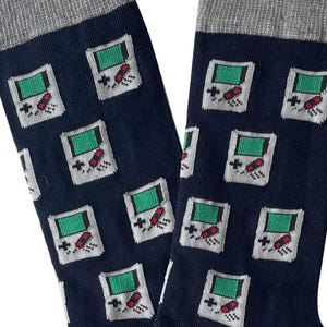May include: A pair of blue socks with a grey cuff. The socks have a repeating pattern of green and white game controllers with red buttons.