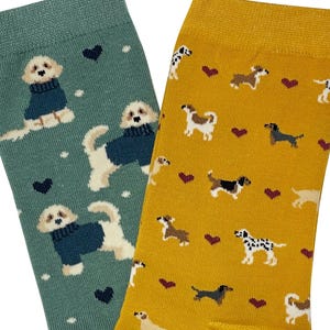 Può includere: Un paio di calzini con un motivo a forma di cane. Un calzino è verde con cani bianchi che indossano maglioni blu e cuori rossi. L'altro calzino è giallo con cani marroni, neri e bianchi e cuori rossi.