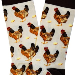 May include: A pair of white socks with a repeating pattern of brown and orange chickens and yellow egg shapes. The socks have a brown cuff and toe. The chickens have red combs and black tail feathers.