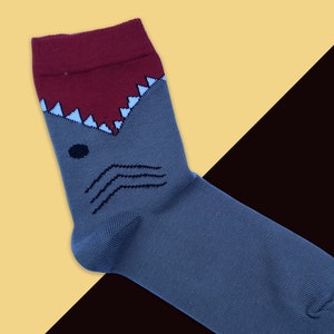 Könnte beinhalten: Graue und rote Haifischsocken mit einem weißen Mund und Zähnen. Die Socken befinden sich auf einem gelben und schwarzen Hintergrund.