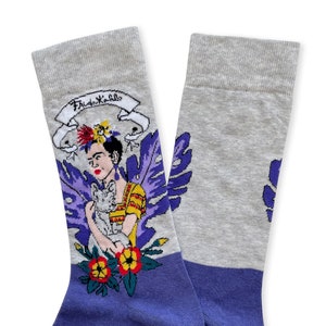 May include: A pair of grey and purple socks with a colorful illustration of Frida Kahlo holding a cat. The socks have the text "Frida Kahlo" on the top of the sock.
