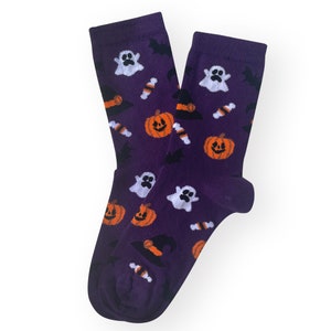 May include: A pair of purple Halloween socks with a repeating pattern of orange jack-o'-lanterns, white ghosts, black bats, candy corn, and witch hats. The socks are made of a soft material and are designed for comfort.