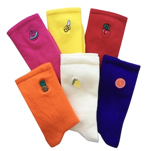 Könnte beinhalten: Sechs Paar bunte Socken mit gestickten Fruchtmotiven. Die Socken sind gelb, rosa, rot, weiß, orange und blau. Die Fruchtmotive umfassen eine Wassermelone, eine Banane, eine Kirsche, eine Zitrone, eine Ananas und eine Orange.