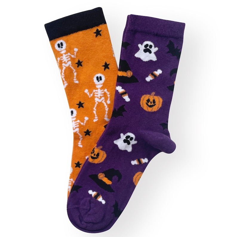 May include: Two Halloween-themed socks. One orange sock features white skeletons and black stars. The other purple sock has ghosts, bats, jack-o'-lanterns, and witch hats. Both socks have black cuffs.