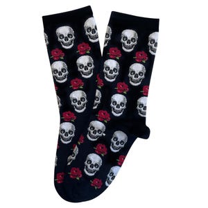 May include: A pair of black socks featuring a repeating pattern of white skulls and red roses. The socks are made of a soft material and are designed to be worn on the feet. The design is a gothic or alternative style.