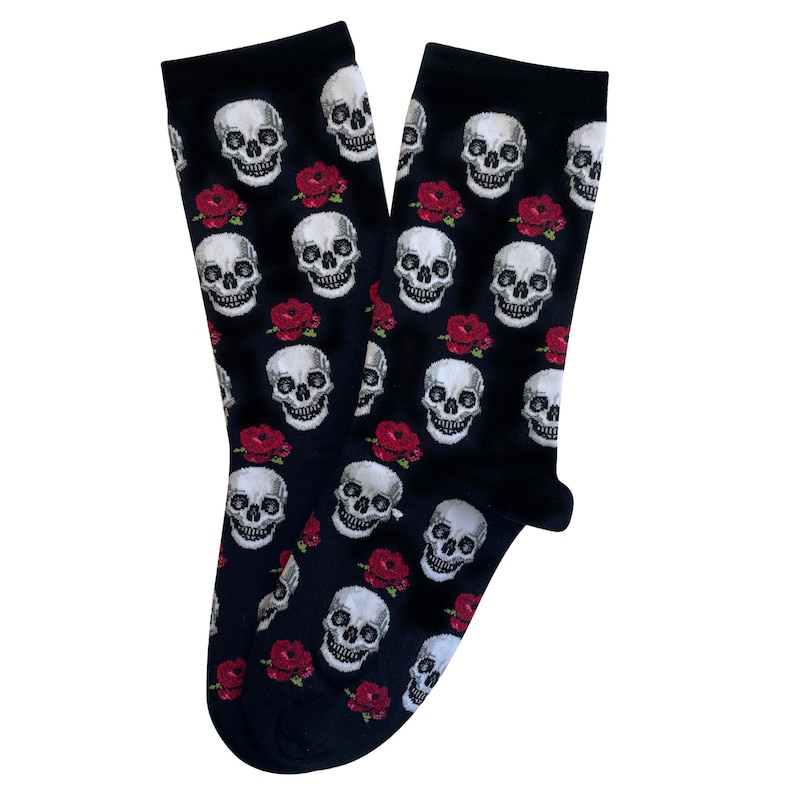 May include: A pair of black socks featuring a repeating pattern of white skulls and red roses. The socks are made of a soft material and are designed to be worn on the feet. The design is a gothic or alternative style.