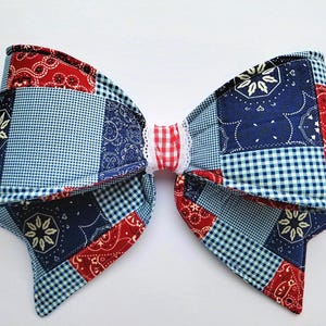 May include: A large, fabric bow featuring a patchwork design in red, white, and blue. The bow's pattern includes paisley, gingham, and floral motifs. The center is a red and white gingham with white lace trim.