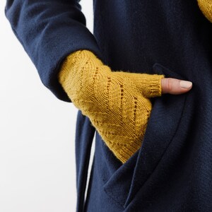 以下が含まれることがあります： マスタードイエローのニット指なし手袋、模様入り。 手袋はネイビーブルーのコートのポケットの中に着用されています。 手袋は柔らかく暖かい素材でできており、寒い季節に最適です。