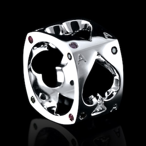 Puede incluir: Un anillo de plata con forma de dado con un pico cortado en el centro. El anillo está decorado con pequeñas piedras preciosas rojas, verdes y negras.